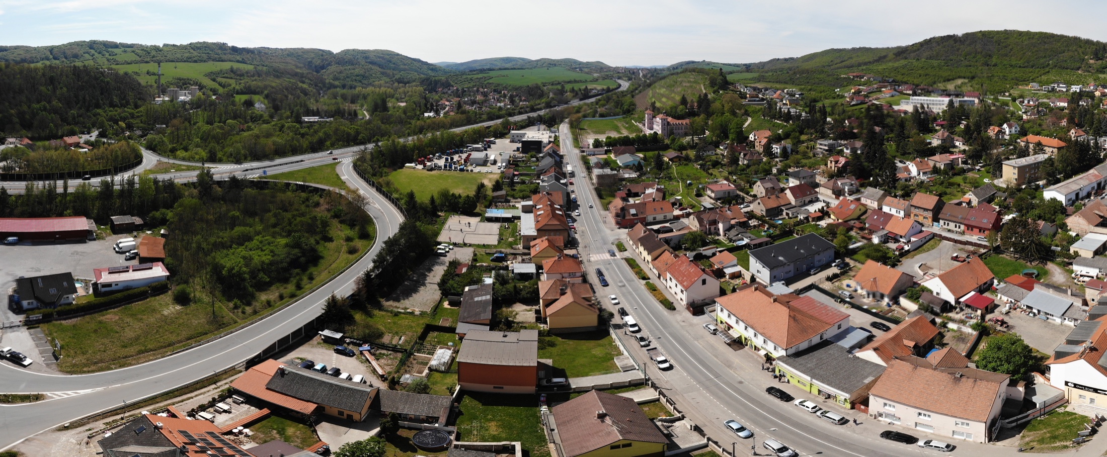 Letecký pohled na Loděnici podél hlavní ulice, v pozadí zalesněné svahy a dálnice D5